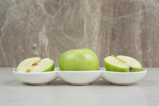 Whole and half cut green apples in white bowls. 