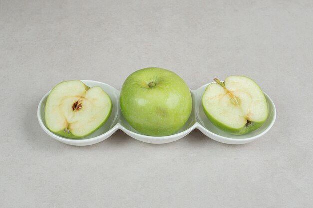 Whole and half cut green apples in white bowls