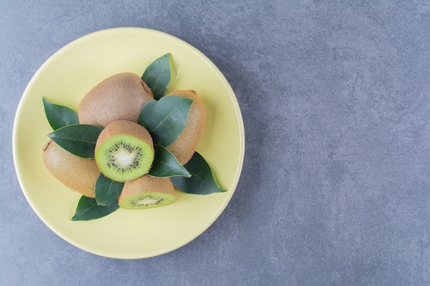 Whole and half kiwi fruits on plate on the dark surface