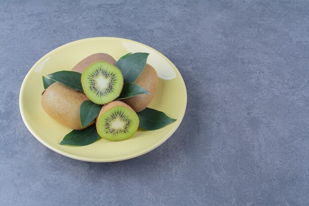 Whole and half kiwi fruits on plate on marble table.