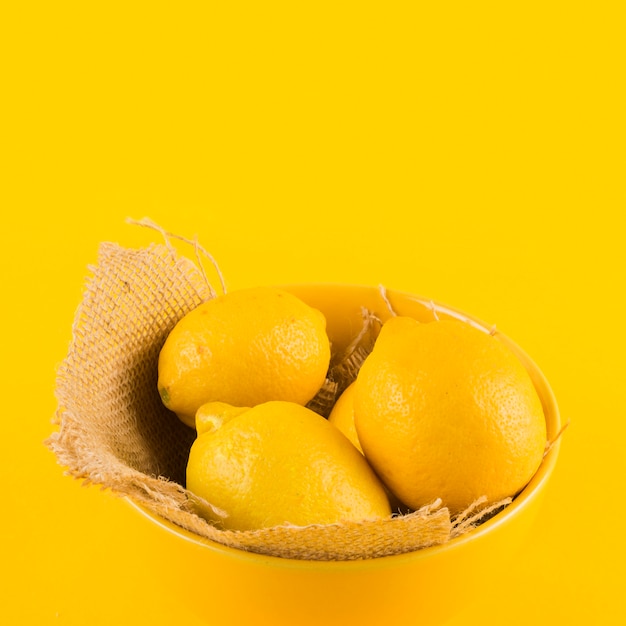 Whole lemon in bowl against yellow backdrop