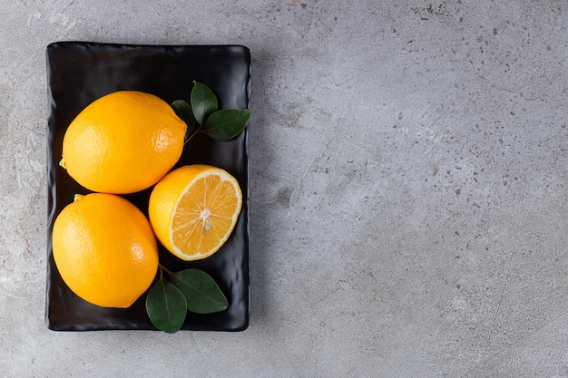 Whole lemons with leaves placed on black plate