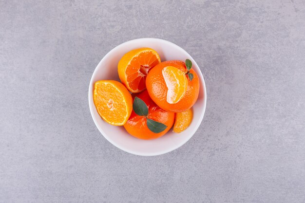 Whole orange fruits with green leaves placed on stone surface.