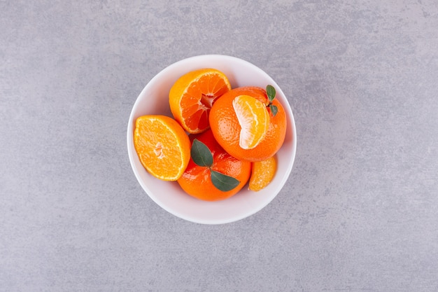 Whole orange fruits with green leaves placed on stone surface.