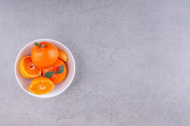 Целые оранжевые плоды с зелеными листьями на белой тарелке.
