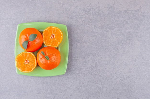 Whole orange fruits with sliced tangerines placed on green plate.