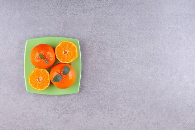 Целые оранжевые плоды с нарезанными мандаринами на зеленой тарелке.