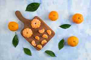 Free photo whole and peeled slice of clementine mandarins. on wooden board over blue surface