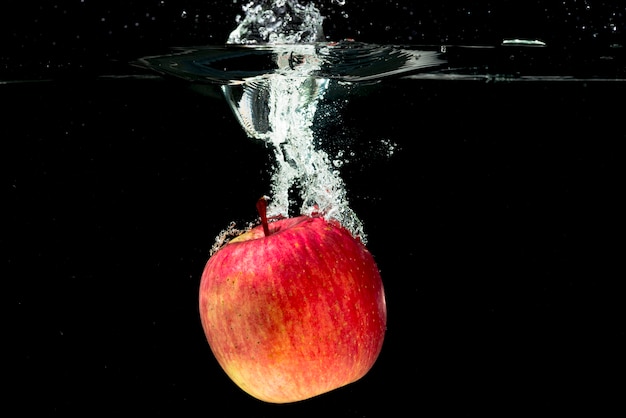 Всего красное яблоко падает в воде на черном фоне