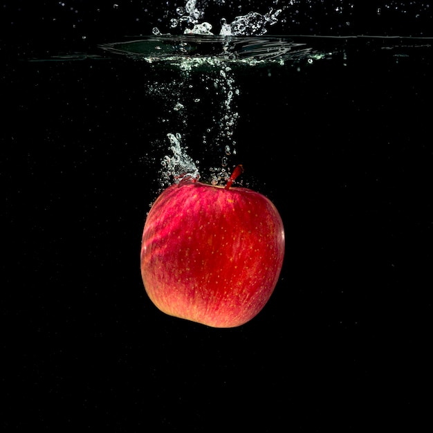 黒の背景に水の中に跳ねる全体の赤いリンゴ