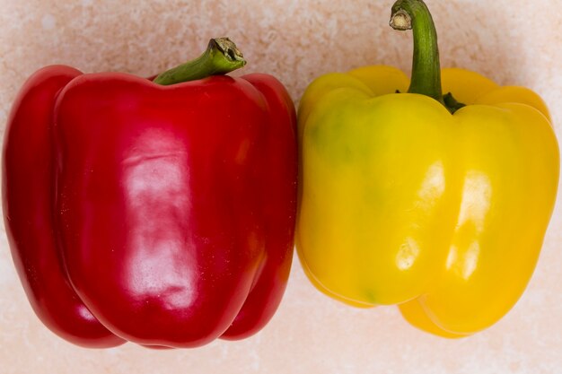 Whole red and yellow bell peppers on textured backdrop