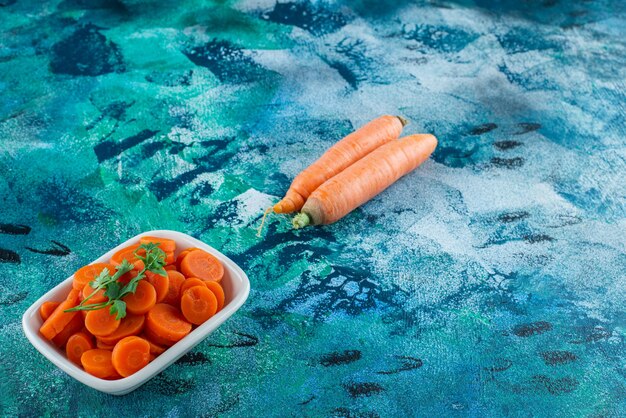 Whole and slice carrots with parsley in a bowl , on the blue table. 