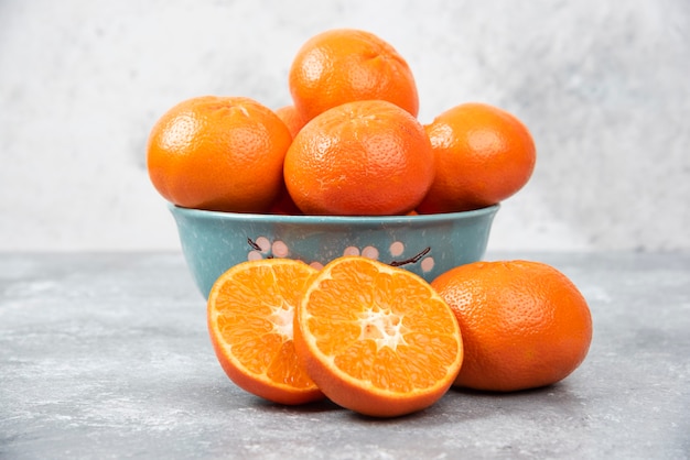 Whole and slice juicy fresh orange fruits in a bowl placed on a stone table .