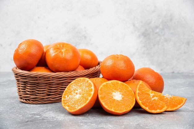 Whole and slice juicy fresh orange fruits in a wicker basket placed on a stone table .