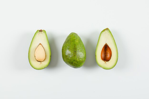 Whole and sliced avocado on a white surface. top view.