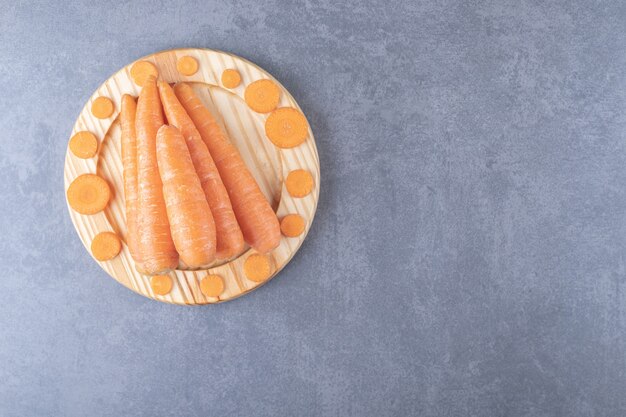 Целая и нарезанная морковь в деревянной тарелке на мраморном фоне.