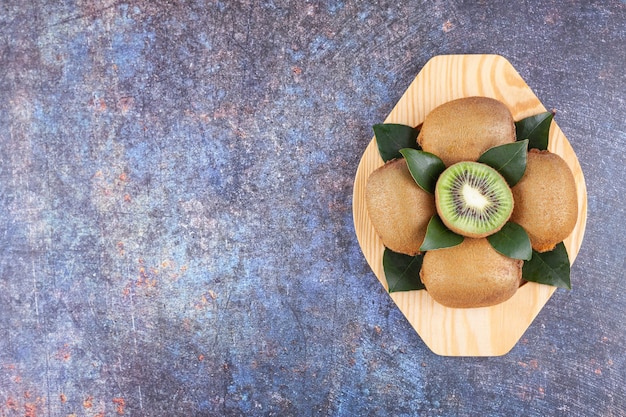 Whole and sliced delicious kiwi with leaves placed on a wooden plate .