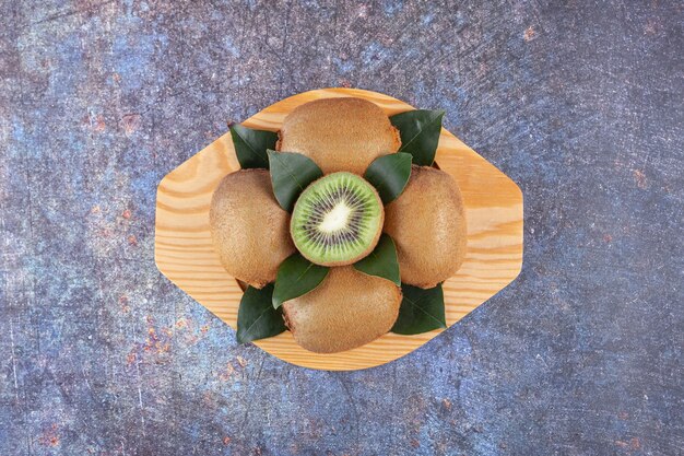 Whole and sliced delicious kiwi with leaves placed on a wooden plate . 