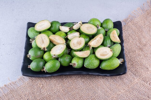 Whole and sliced feijoas on a platter on marble background. High quality photo