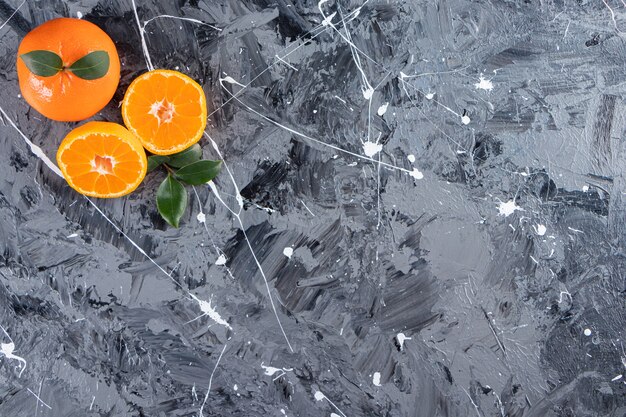 Whole and sliced fresh orange fruits with leaves placed on a marble table.