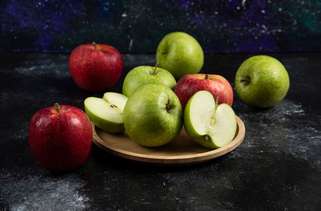 Whole and sliced green and red apples on wooden plate. 