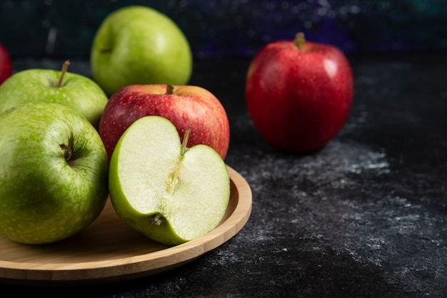 Free photo whole and sliced green and red apples on wooden plate.