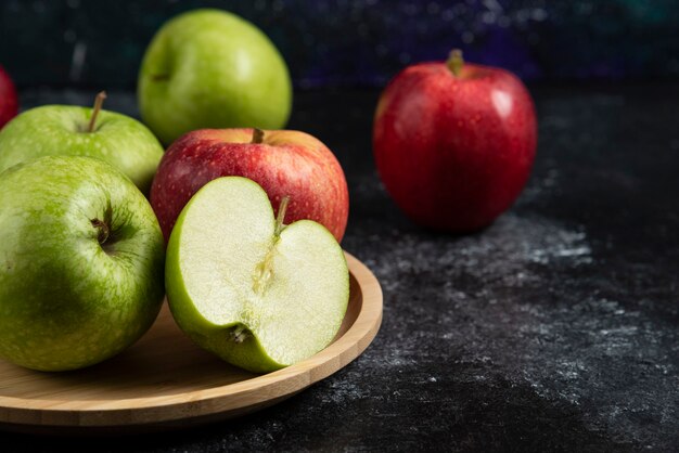 Whole and sliced green and red apples on wooden plate. 