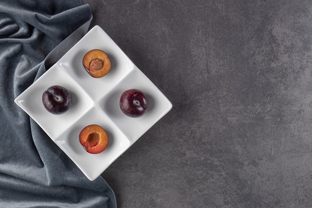 Free photo whole and sliced juicy red plum fruits placed on a white plate.