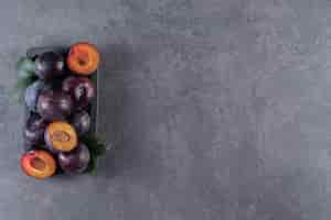 Free photo whole and sliced juicy red plum fruits placed on a wooden board