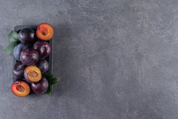 Whole and sliced juicy red plum fruits placed on a wooden board