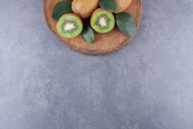 Whole and sliced kiwi fruit placed on a stone table.