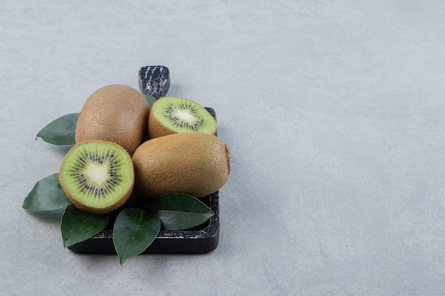 Whole and sliced kiwis on black cutting board. 