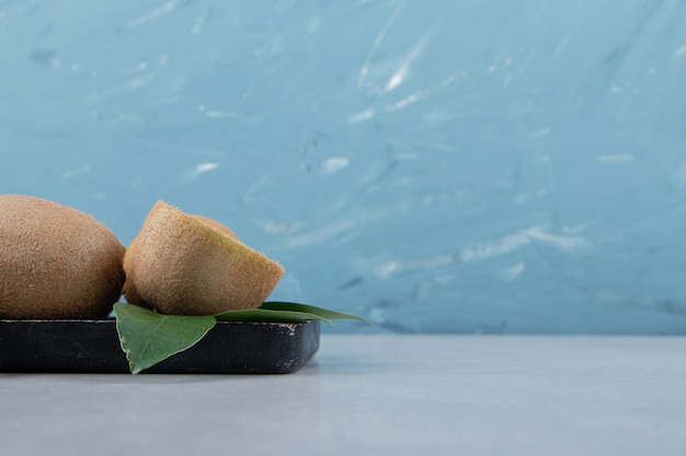 Whole and sliced kiwis on black cutting board