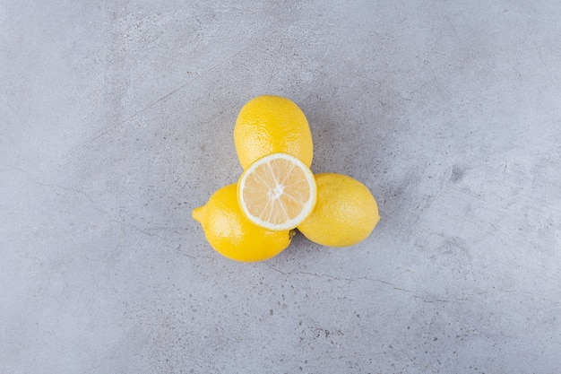 Frutti di limone interi e affettati con foglie poste sul tavolo di pietra.