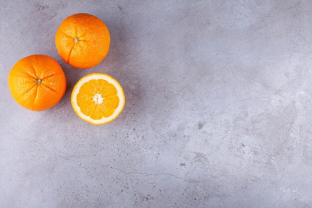Whole and sliced orange fruits placed on a stone background . 