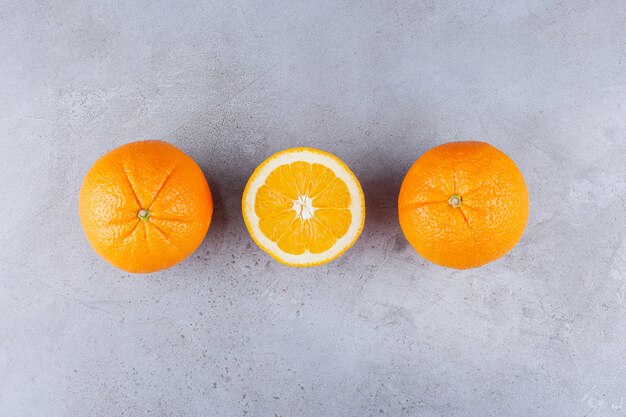 Целые и нарезанные апельсиновые плоды на каменном столе.