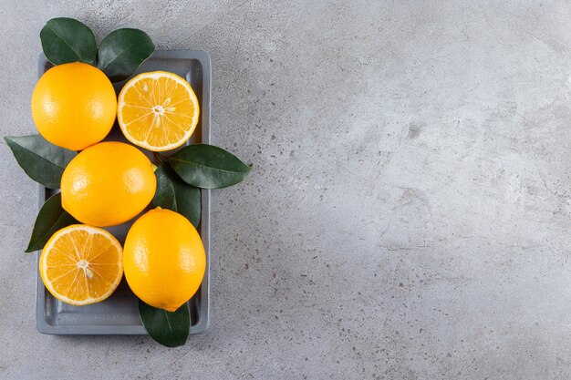 Whole and sliced oranges with leaves placed on board.