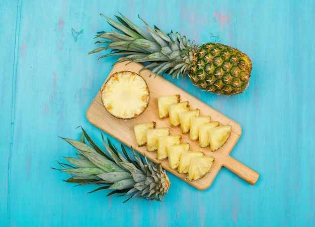 Foto gratuita ananas intero ed affettato in una vista superiore del tagliere su un ciano blu