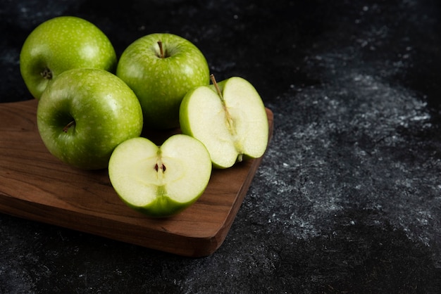 Whole and sliced ripe green apples on wooden board. 