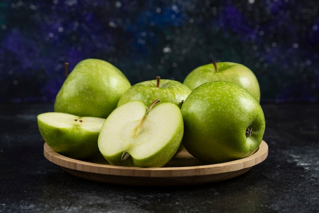Whole and sliced ripe green apples on wooden plate. 