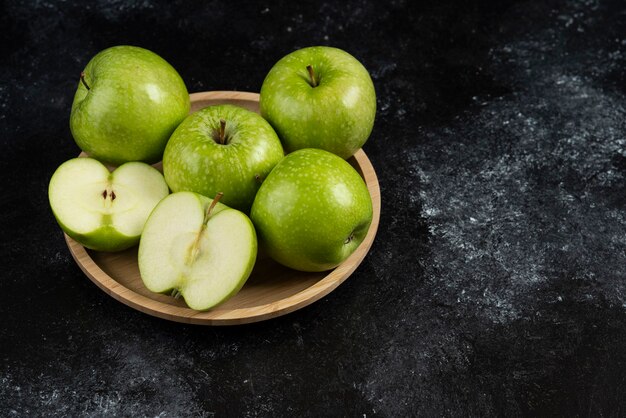 Free photo whole and sliced ripe green apples on wooden plate.