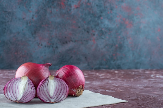 Whole and sliced ripe onion on a pieces of fabric on the marble surface