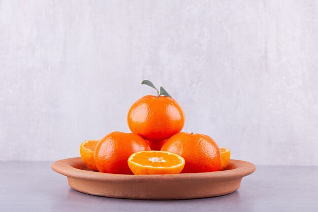 Целые и нарезанные плоды мандарина с листьями на каменном столе.