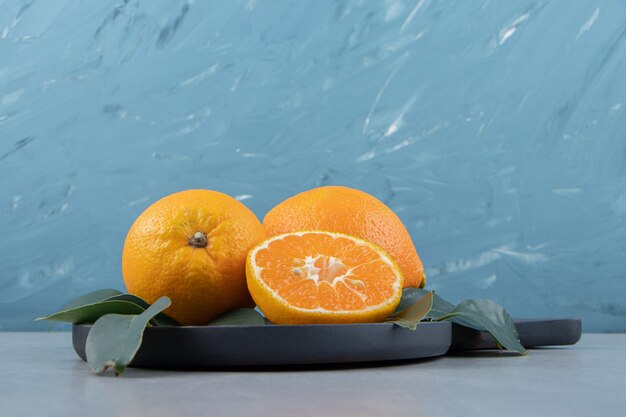 Whole and sliced tangerines on black cutting board. 