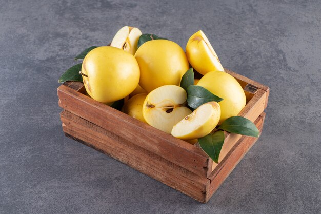 Целые и нарезанные плоды желтого яблока с листьями на деревянном ящике.