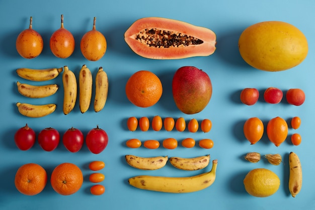 Whole and slices of exotic fruits isolated on blue studio background. Cumquat, bananas, red fortunella, yellow mango, lemons, peaches, physalis. Creative summer composition. Essential nutrition