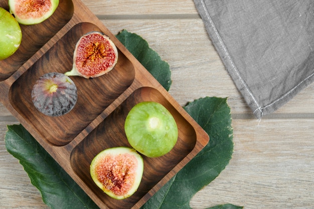 Free photo whole and slices of green and black figs on wooden platter with a leaf and a tablecloth.