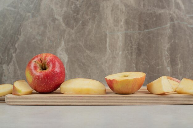 Whole and slices of red apple on wooden board