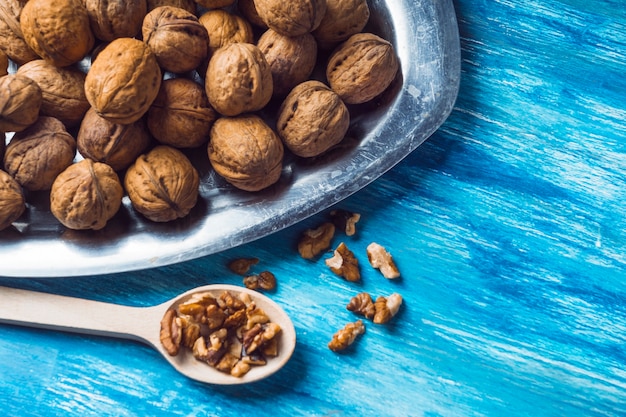 Whole walnuts and kernel on tray and wooden spoon on blue painted backdrop