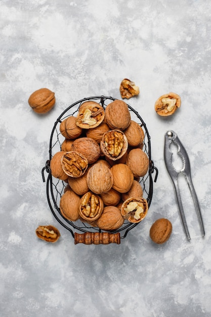 Whole walnuts in shell in food metal basket, walnut kernels. Top view on concrete 